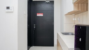 A black door with a sign, a white wall-mounted device, a kitchen area with a sink, and a purple patterned cabinet. - Simply Strategic and Comfy Studio Paramount Skyline Apartment (Gading Serpong)