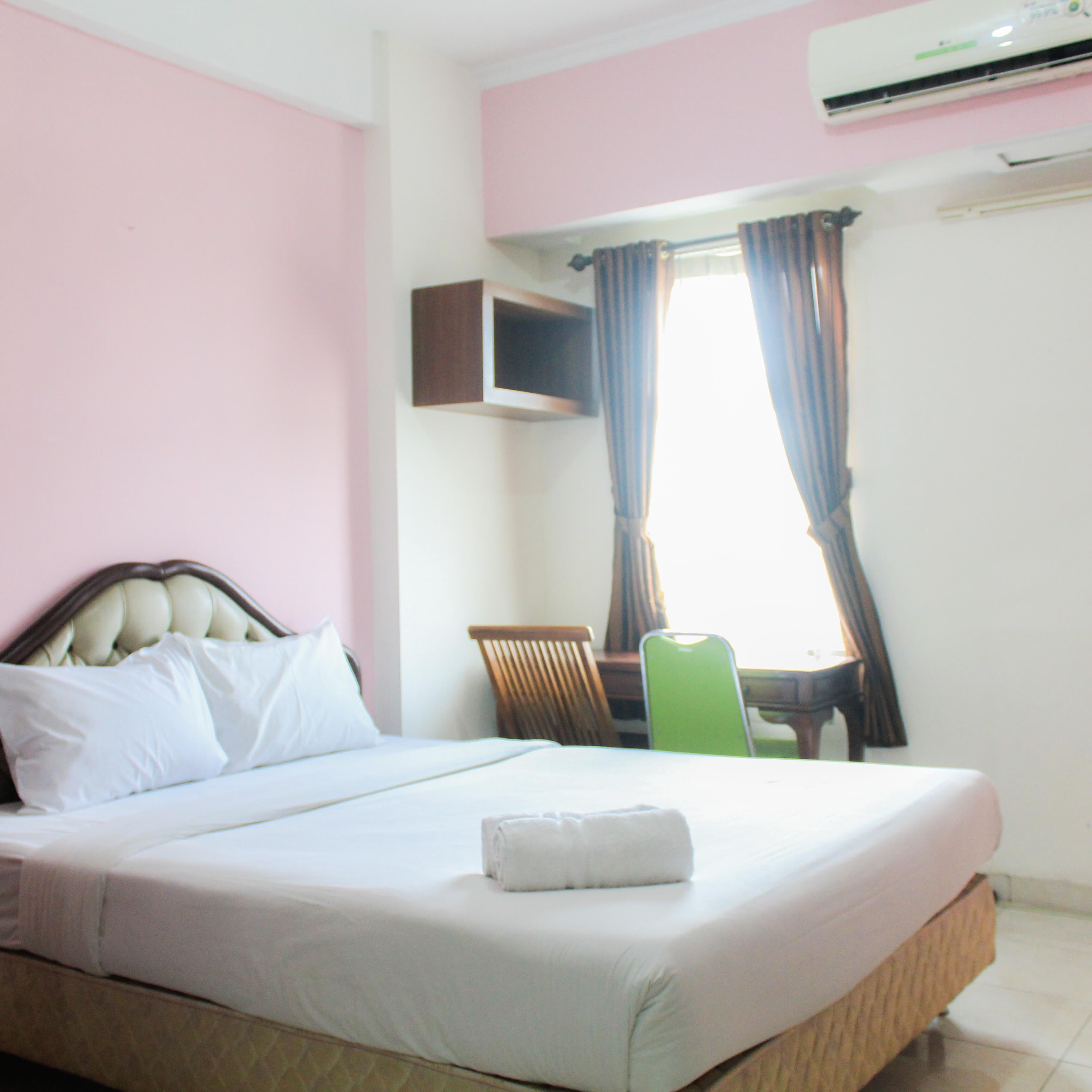 Una cama bien hecha con almohadas, una silla verde y un televisor montado en la pared.