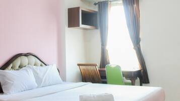Una cama bien hecha con almohadas, una silla verde y un televisor montado en la pared.