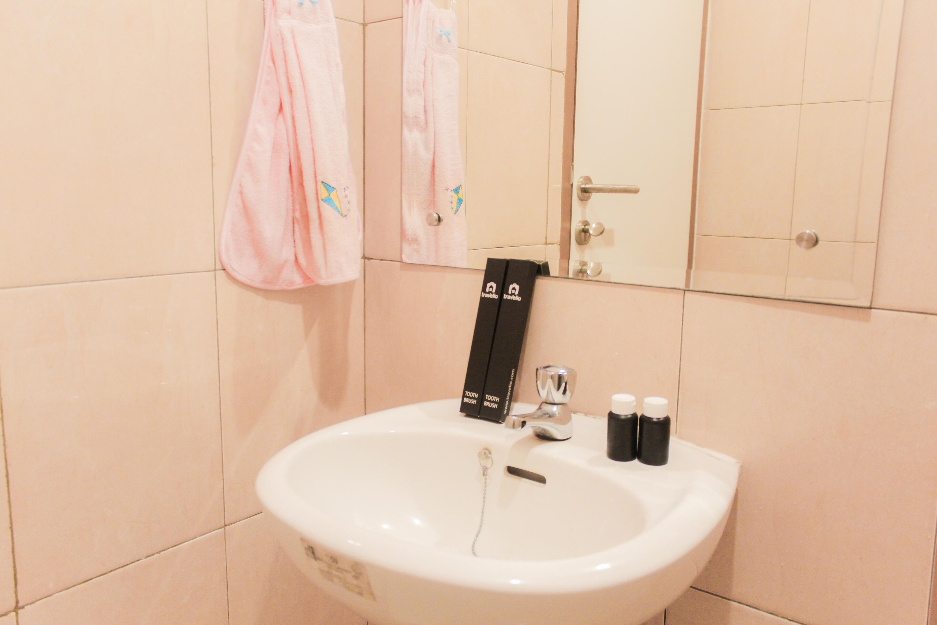 Un bagno con un lavandino bianco, uno specchio e due asciugamani rosa appesi al muro.