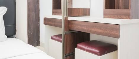 Una habitación de hotel con una cama, un tocador de madera con espejo y un banco rojo.