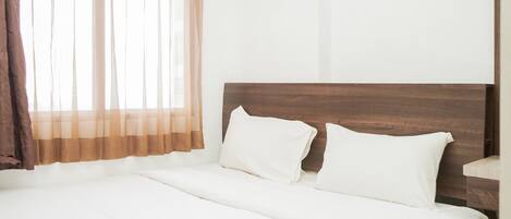 A neatly made bed with white linens and two pillows, a wooden headboard, and a window with sheer curtains.