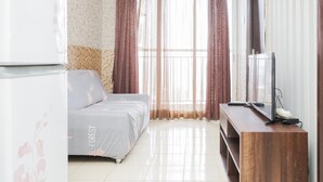Une chambre à coucher avec un lit, un téléviseur posé sur un meuble en bois et des rideaux en voile.