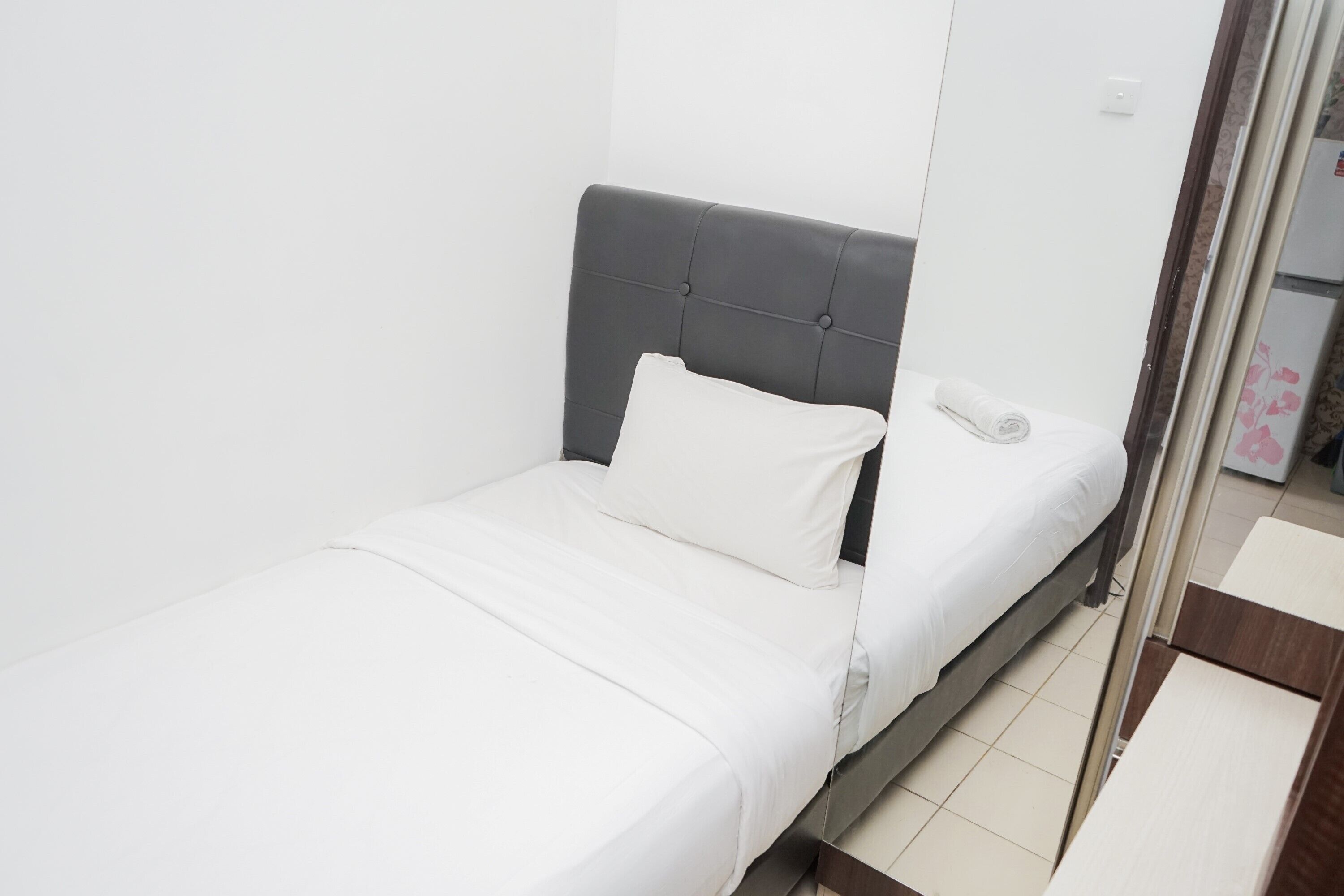 Una cama individual con cabecera tapizada en gris, ropa de cama blanca y un teléfono en la mesita de noche.