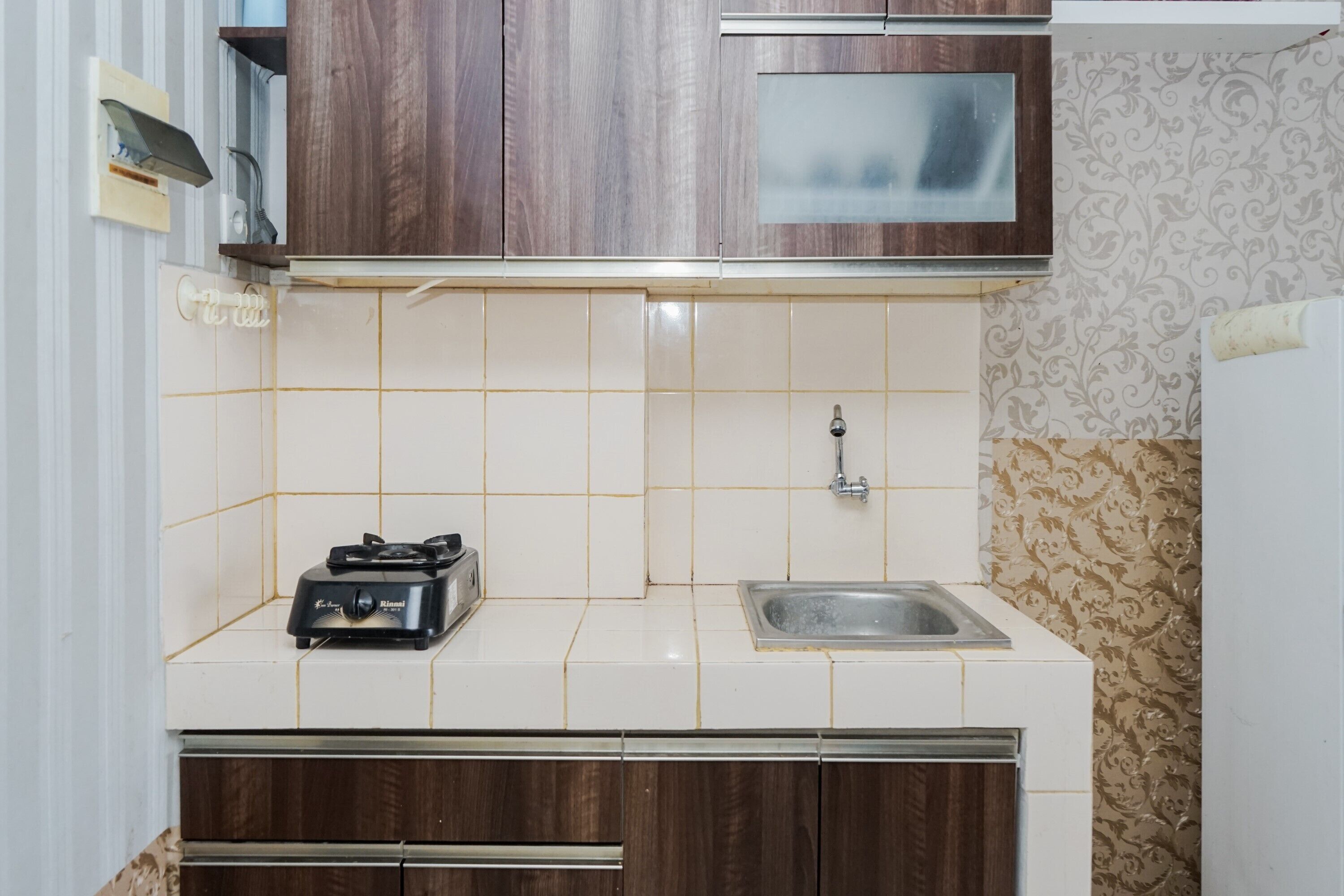 A kitchen with white tiles, a stainless steel sink, and wooden cabinets.