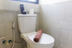 A toilet with a towel on the seat, a toilet paper holder, and a bidet attachment. - Homey and Enjoy 2BR at Meikarta Apartment (Cikarang)