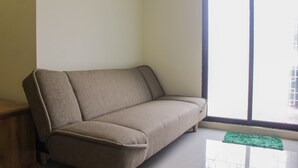 A living room with a sofa, a small rug, and a window with a view of buildings. - Homey and Enjoy 2BR at Meikarta Apartment (Cikarang)