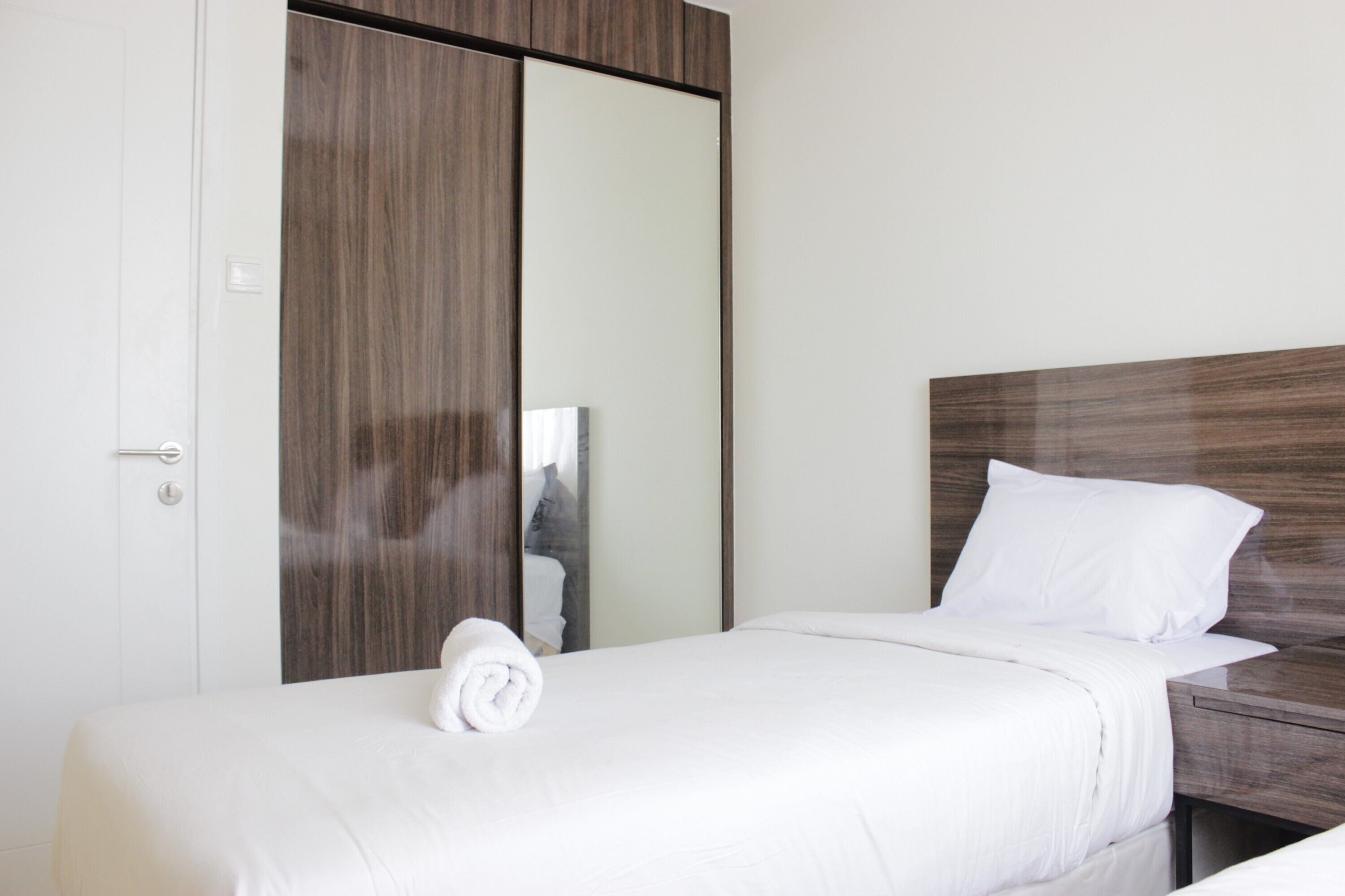 A hotel room with a wooden wardrobe, a bed with white linens, and a nightstand.