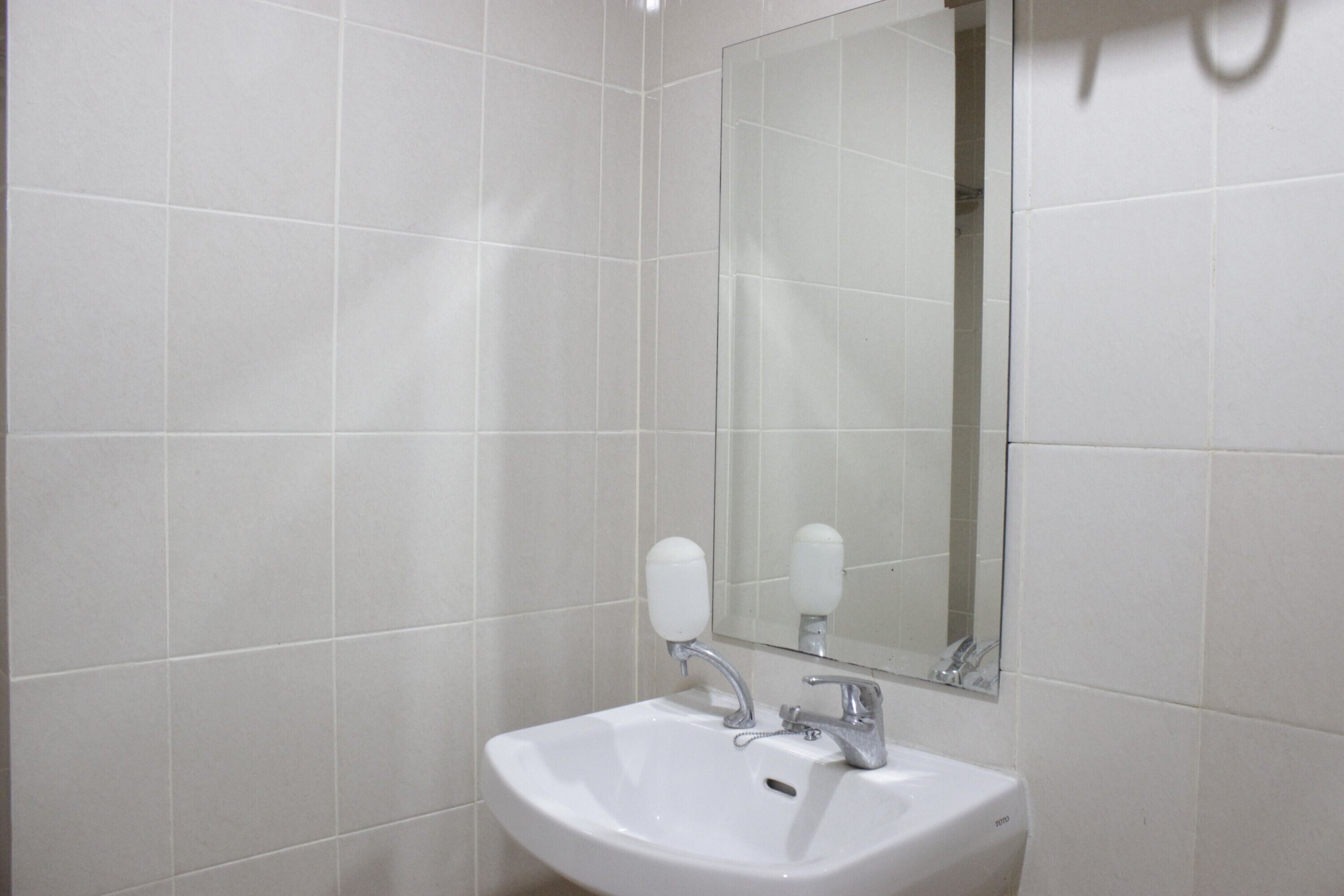 A bathroom with white tiles, a sink, and a mirror.