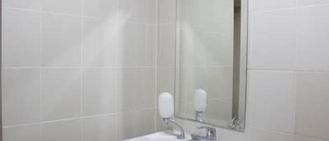 Un baño con azulejos blancos, un lavabo y un espejo.