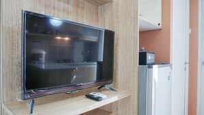Ein Flachbildfernseher auf einem Holzboden in einem Raum mit einem weißen Kühlschrank und einem Holzschrank.