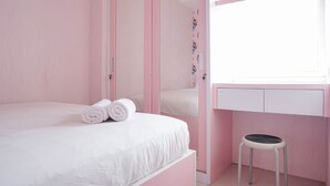 Ein zartrosa Schlafzimmer mit einem Bett, einem kleinen Hocker und einem Fenster.