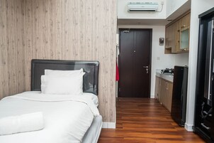 A hotel room with a bed, wooden panel walls, a kitchen area with cabinets and appliances, and a door leading to another room.