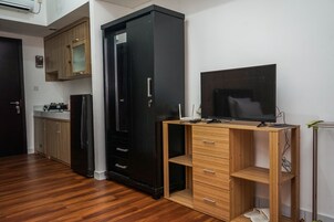 Una cocina compacta con armarios de madera, un refrigerador negro y un escritorio de madera con televisor de pantalla plana.