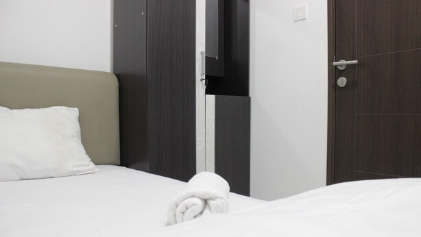 Un lit bien fait, avec un oreiller blanc et une serviette pliée, une armoire en bois et une porte dotée d’une poignée.