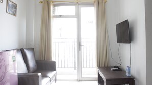 Une pièce comprenant un canapé, une table avec un téléviseur et une télécommande, une bouteille d’eau et une porte-fenêtre coulissante donnant sur un balcon.
