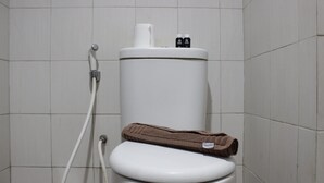 Des toilettes avec un abattant et un couvercle blancs, une serviette marron et un porte-rouleau de papier toilette.