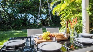 An outdoor dining table set with plates, cutlery, glasses, a bottle, and a fruit platter.