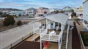 A coastal residential area with multi-story houses, a covered outdoor seating area, and a sandy beach in the background. - Adorable Ocean View 3 Bed/1 Bath Cottage Sleeps 8 steps to the beach (Ocean Isle Beach)