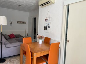 A dining area with a wooden table and orange chairs, a grey sofa, and a white wall with a picture frame and wall art.