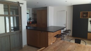 A kitchen with wooden cabinets, a black countertop, and a dining area with a wooden table and chairs. - Maison à la Campagne 15min de la mer (Beaulieu-Sous-la-Roche)