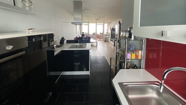Una cocina moderna con gabinetes blancos y negros, un lavamanos de acero inoxidable y una pared de acento roja.