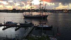 Un puerto con un gran barco de vela amarrado, embarcaciones más pequeñas y una noria al fondo.