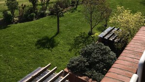 Vista de una zona verde con una masa de agua al fondo, un sendero pavimentado y una estructura de ladrillo con techo.