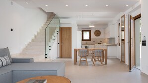 A modern living room with a sofa, a coffee table, and a staircase leading to a kitchen area. - De.Light Boutique Villa I, close to Rethymno (Atsipopoulo)