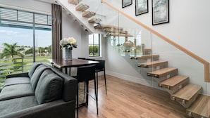 Un salon moderne doté d’un escalier en verre, d’un coin repas et offrant une vue sur l’extérieur.