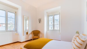 Una camera da letto con un letto, due finestre, una sedia e un quadro appeso al muro.
