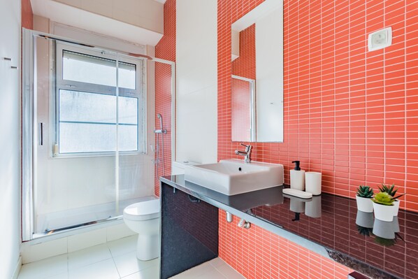 A modern bathroom with a glass shower enclosure, a white sink, and red-tiled walls.