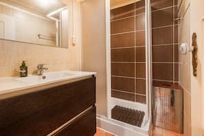 Een badkamer met een houten wastafelmeubel, een witte wastafel, een spiegel en een douchegedeelte met bruine tegels.
