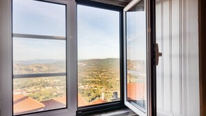 Ein Fenster mit Blick auf eine hügelige Landschaft und Gebäude.