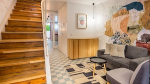 Eine Treppe mit Holzbodenstufen führt zu einem Raum mit einem Schachbrettmuster-Boden, einem grauen Sofa und einem Wandgemälde.