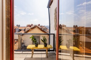 A balcony with a table and potted plants, overlooking a cityscape with traditional buildings. - Victorias Studios - Clérigos (Porto)