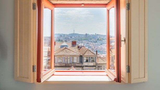 Ein offenes Fenster mit Blick auf eine Stadtlandschaft, einschließlich Gebäude und einem entfernten Turm.