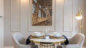 A dining area with a round table set for two, a framed architectural painting on the wall, and a modern floor lamp. - Santa Catarina Prime Studios (Porto)