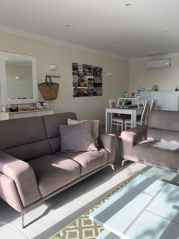 Ein Wohnzimmer mit einer Couch, einem Esstisch mit Stühlen, einer Wand-Klimaanlage und einem Wandbild.