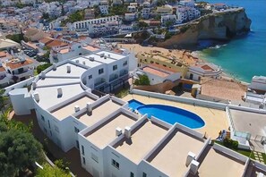 A residential building with a rooftop swimming pool, white exterior, and a view of the coastline.