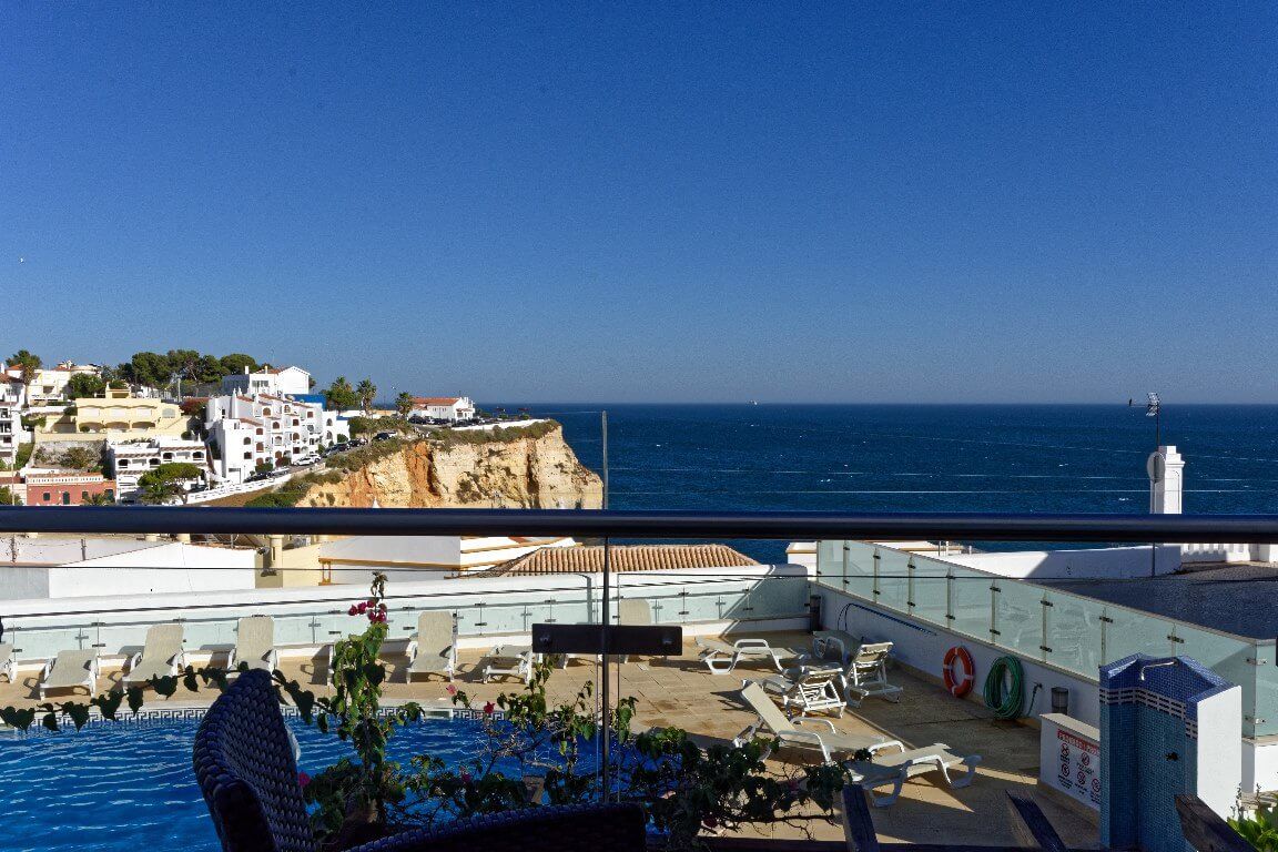 Zona de piscina en la azotea con sillones de descanso y vista al mar y edificios.