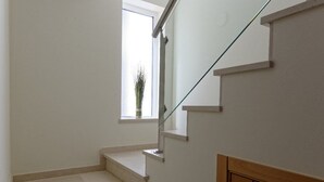 A staircase with a glass railing, a window with a plant, and a wooden panel on the wall. - Apartment Oasis Praia Carvoeiro Bay (Lagoa)