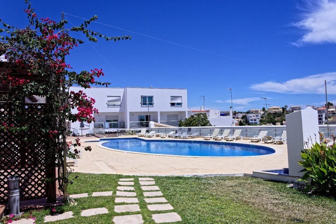 Un edificio moderno con piscina, sillones de descanso y cielo despejado.