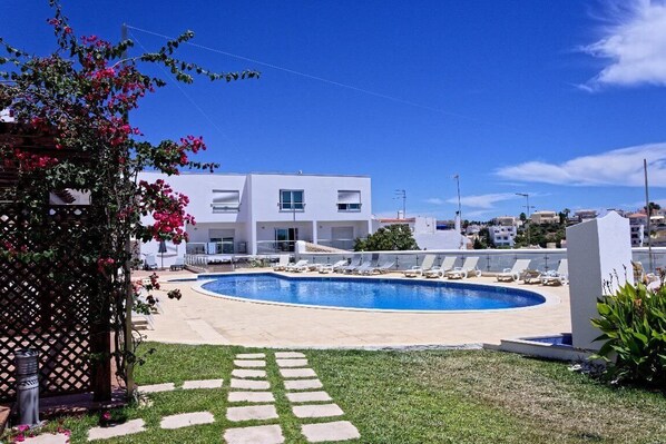 A modern building with a swimming pool, lounge chairs, and a clear sky.