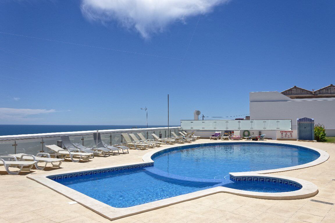 Una piscina con sillones de descanso, vista al océano y un edificio de techo plano.