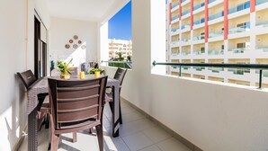 A balcony with a dining table and chairs, a railing, and a view of a multi-story building. - Quinta das Palmeiras Pool & Beach in Pêra (Lagoa)