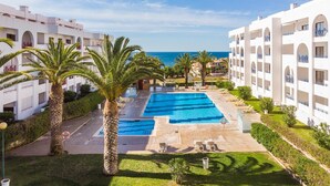 A resort with a central swimming pool, palm trees, and a view of the sea. - Quinta das Palmeiras Pool & Beach in Pêra (Lagoa)