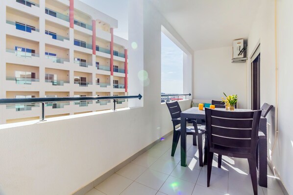 A balcony with a view of a multi-story building, a table with chairs, and a clock on the wall. - Quinta das Palmeiras Pool & Beach in Pêra (Lagoa)