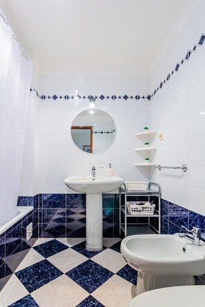 A bathroom with a white sink, a round mirror, and a bidet. The floor has a black and white checkered pattern. - Quinta das Palmeiras Pool & Beach in Pêra (Lagoa)