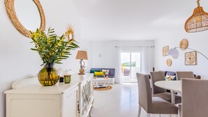 A bright, modern living room with a white sofa, a dining table, and a large window. - Happy House in Clube Albufeira (Albufeira)